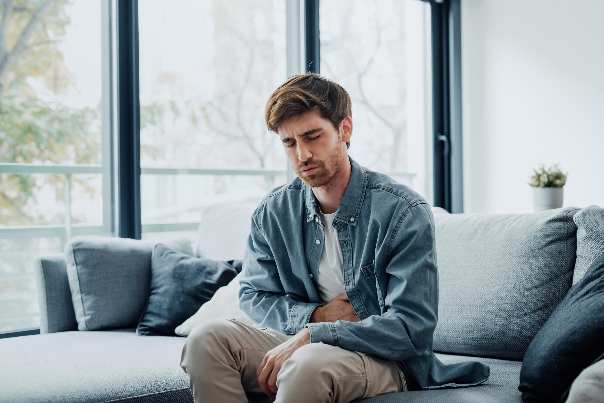 Person sitting, holding stomach in discomfort.